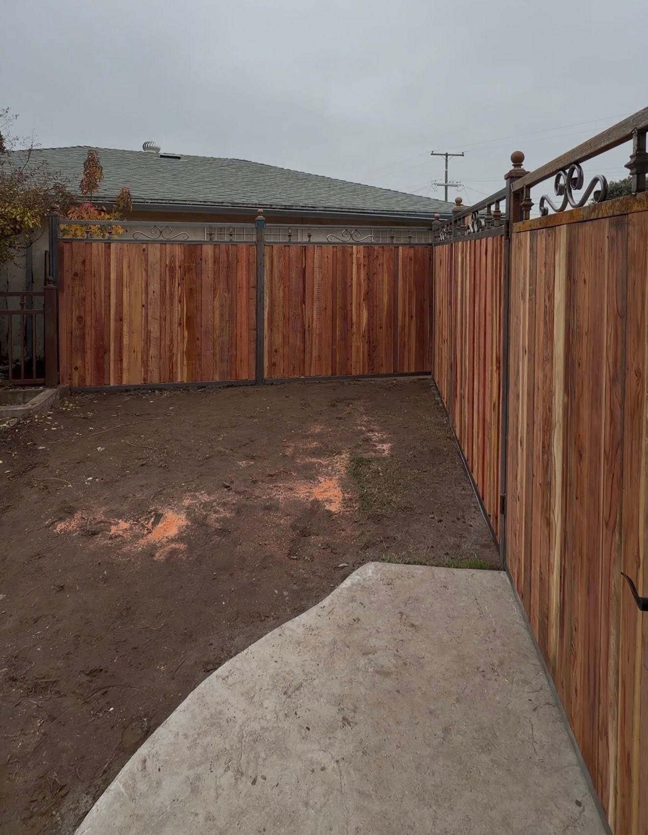 Small fenced backyard with redwood fence, bare dirt, and a concrete patio corner