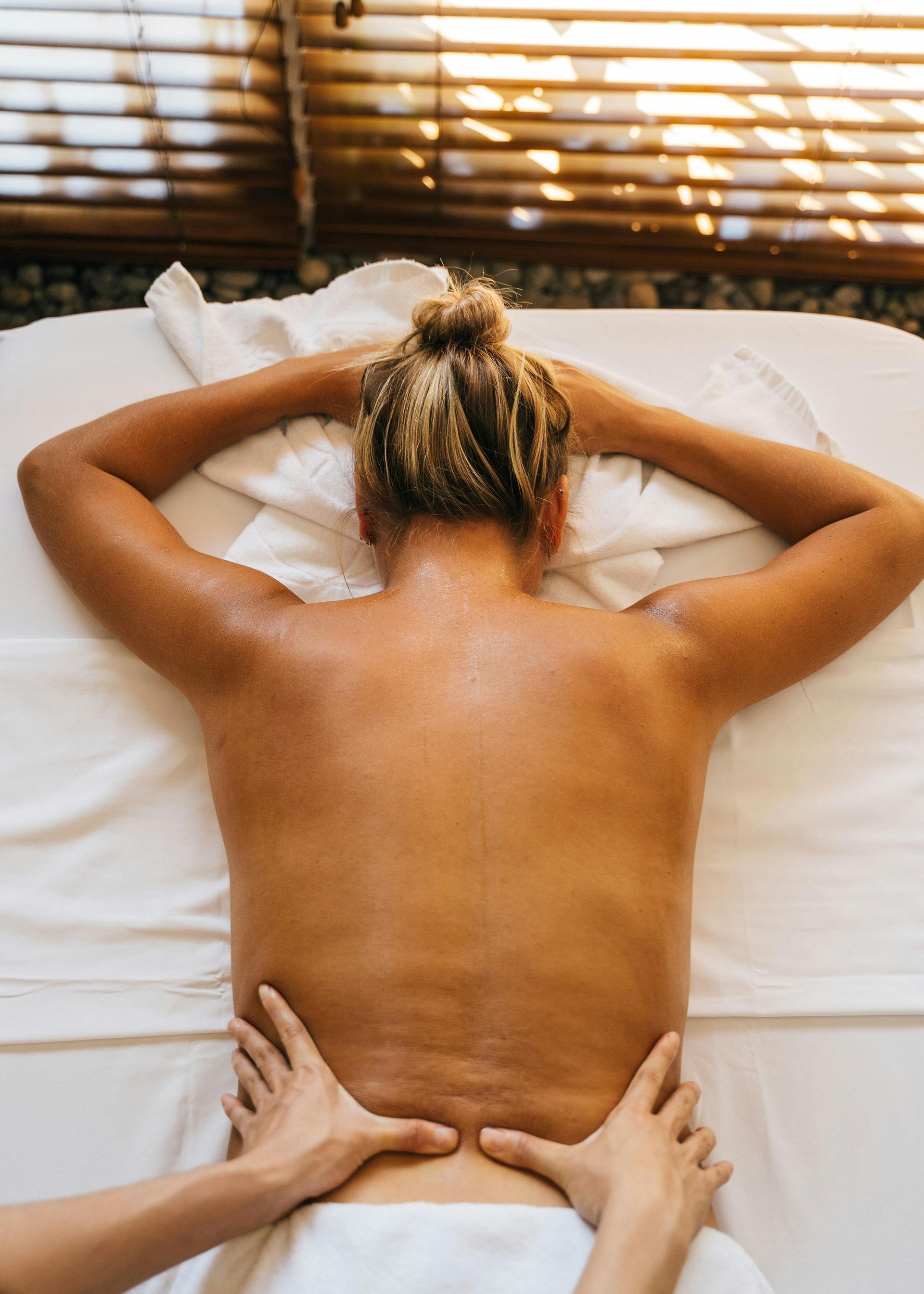 Person receiving a massage on a white sheet, hands kneading lower back.