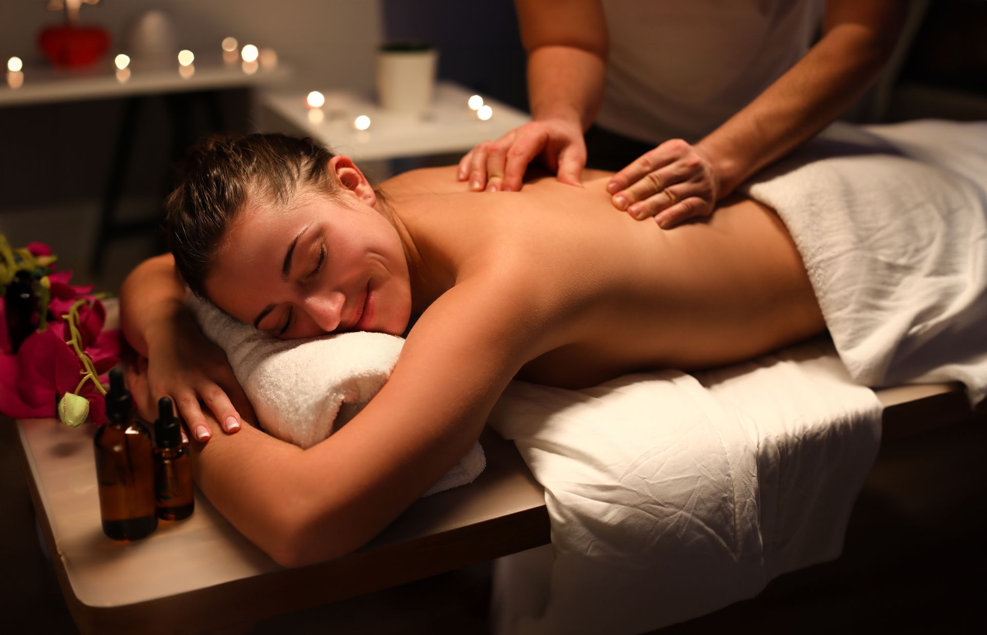 Woman receiving back massage, relaxed expression. Spa setting, dim lighting, candles.