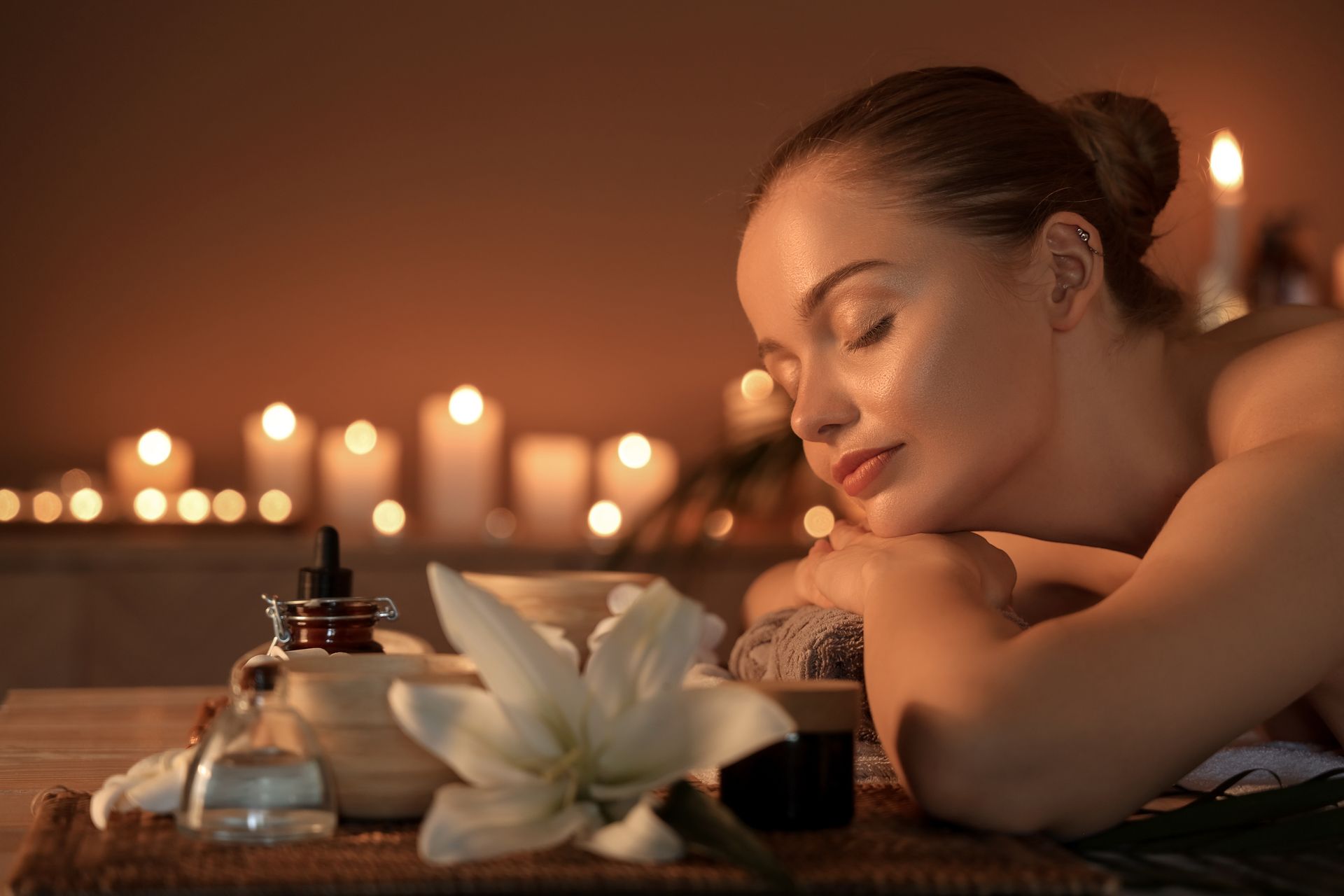 Woman relaxing at spa with candles and essential oils.