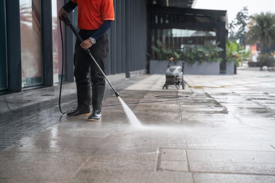 A Man is Using a High Pressure Washer to Clean a Sidewalk — Derek's Dirty Deeds In Howard, QLD