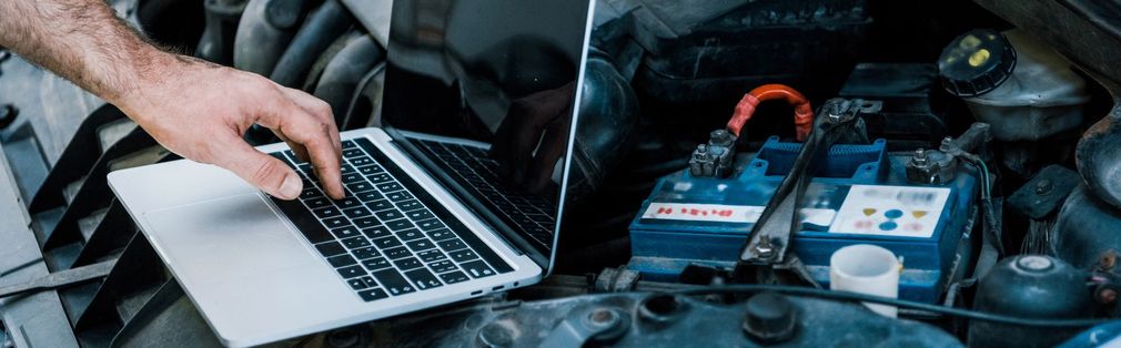 Meccanico che utilizza un computer portatile mentre lavora sulla batteria di un'auto nel vano motore.