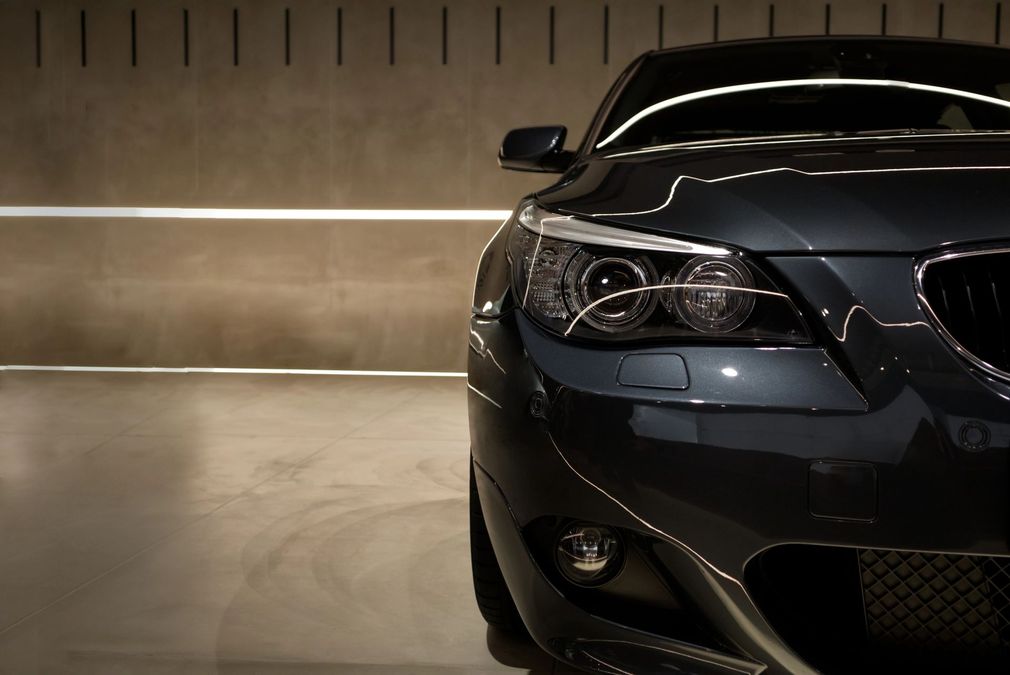 Auto grigio scuro, vista frontale, all'interno di un garage con illuminazione calda.