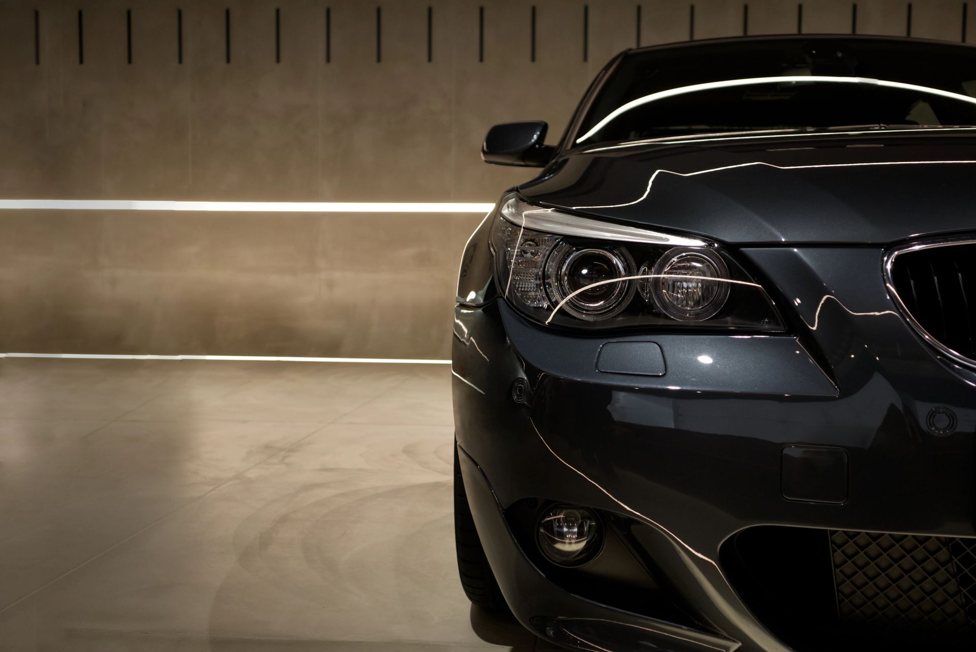 Auto grigio scuro, vista frontale, all'interno di un garage con illuminazione calda.