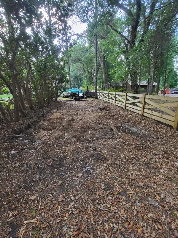 A wooden fence surrounds a dirt road surrounded by trees.
