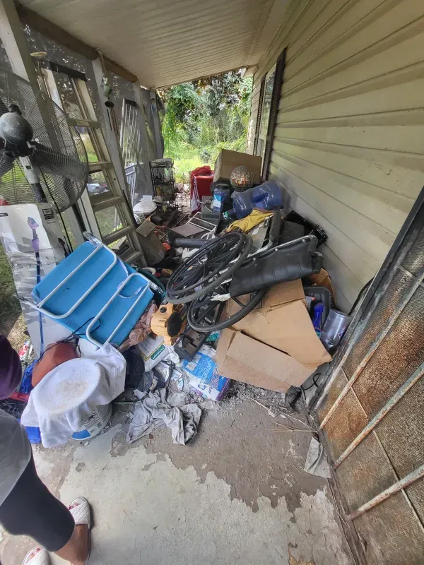 A woman is standing in front of a house covered in trash.