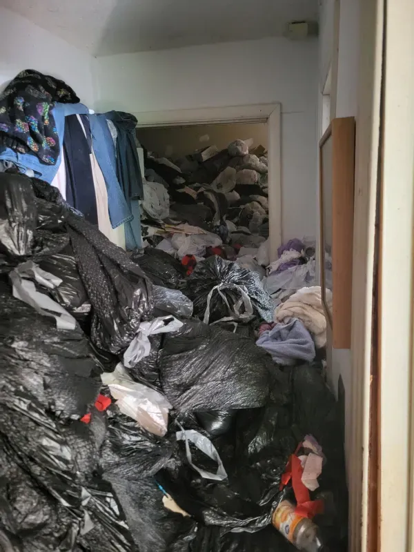 A room with a lot of trash bags and clothes on the floor.