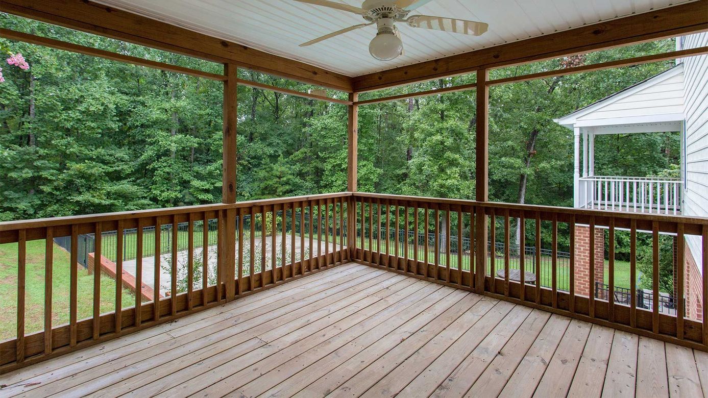 A screened in porch with a ceiling fan and trees in the background.