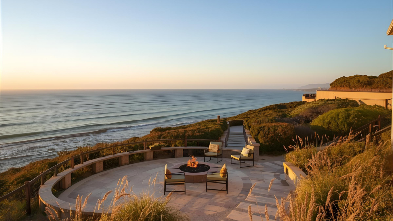 Coastal patio with fire pit, chairs, and ocean view at sunset.