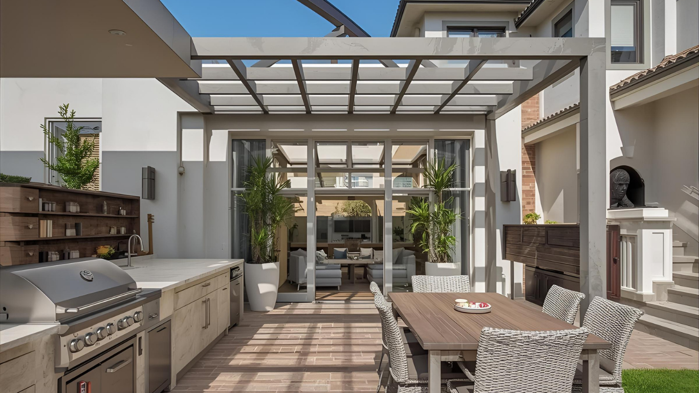 Outdoor kitchen and dining area with a grill, table, and pergola.