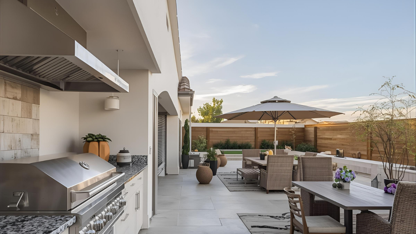 Outdoor kitchen with grill, dining set, and umbrella on a patio.