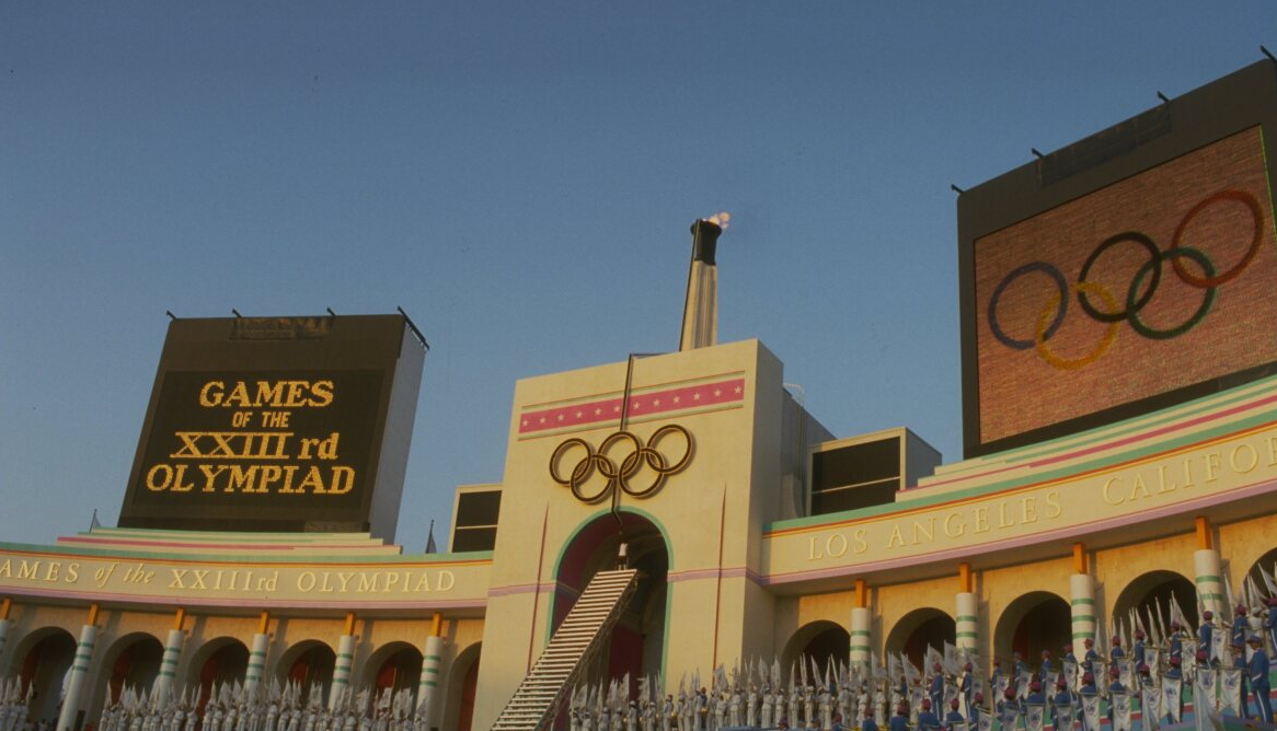 Los Angeles Memorial Coliseum at the 1984 Olympics. Stadium facade with Olympic rings and torch against a blue sky.