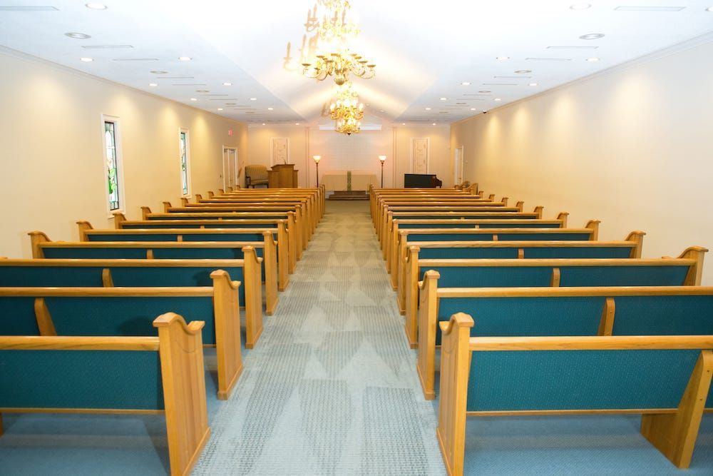 Interior of a funeral home chapel with rows of wooden pews and a chandelier.