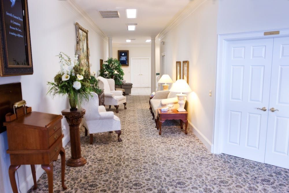 Hallway with seating, floral arrangement, and a desk; neutral tones, white walls, and patterned carpet.