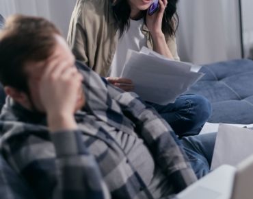A man is sitting on a couch while a woman talks on a cell phone.