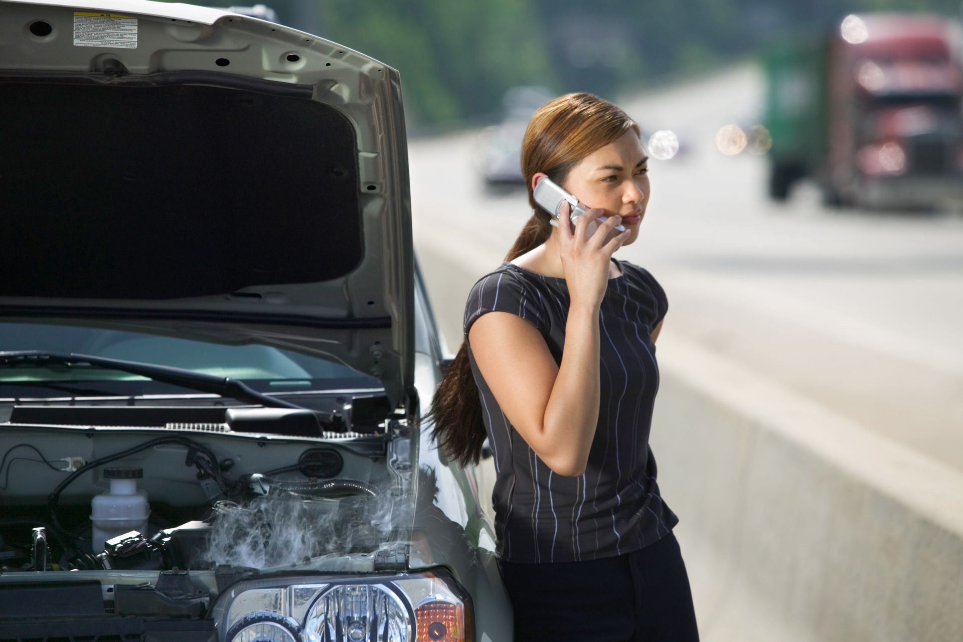 A woman is talking on a cell phone next to a broken down car.
