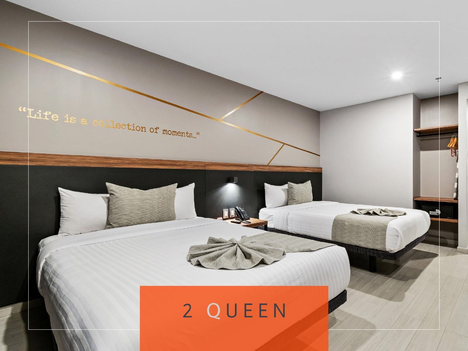 Habitación de hotel con dos camas queen, decoración en gris y blanco, cita en la pared y una etiqueta de texto naranja que dice 