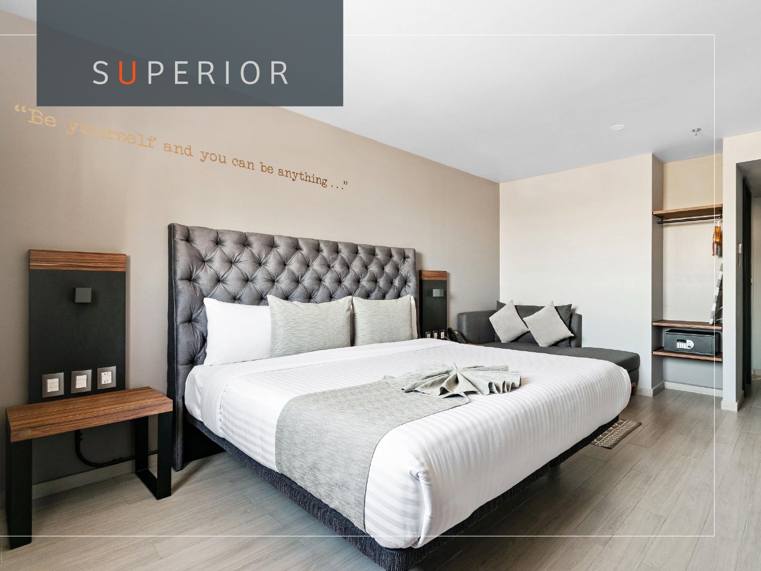 Habitación de hotel con cama grande, sofá y armario; colores neutros, diseño moderno.