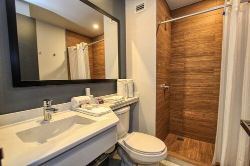 Baño con espejo rectangular, lavabo blanco, inodoro y ducha a ras de suelo con azulejos imitación madera.