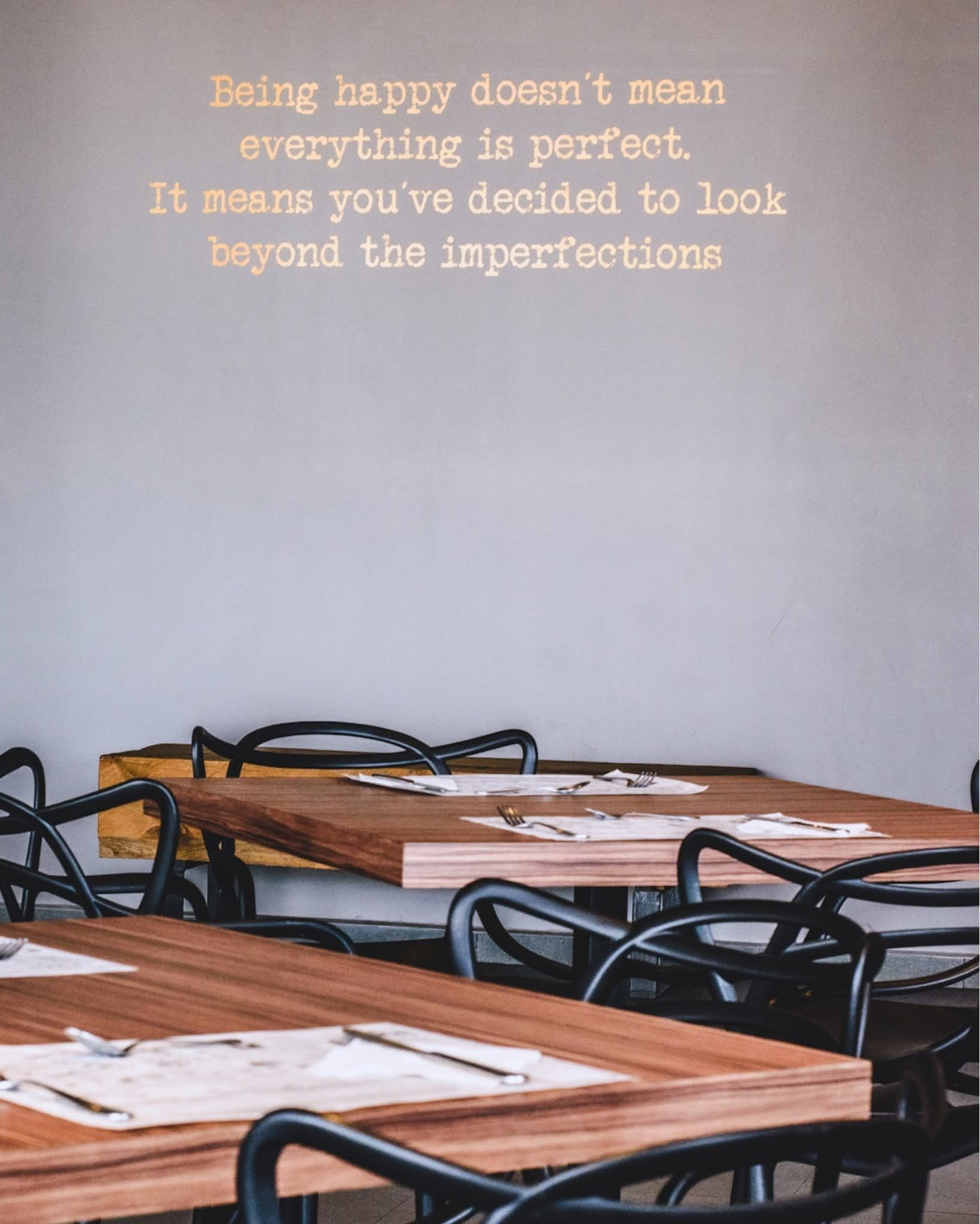Mesas de madera y sillas negras en un restaurante, con texto en la pared: 
