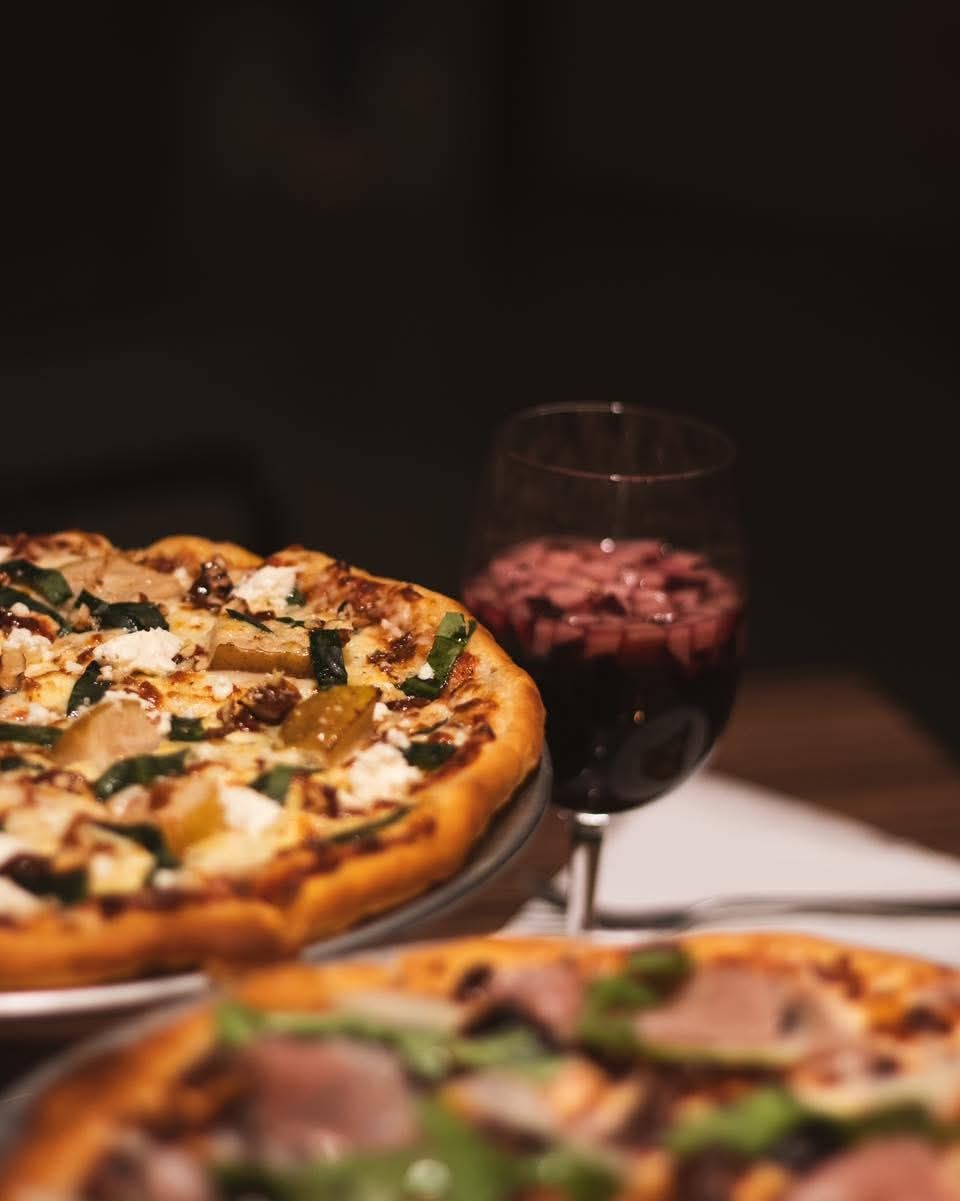 Pizza y una copa de vino tinto sobre una mesa, enfoque suave.