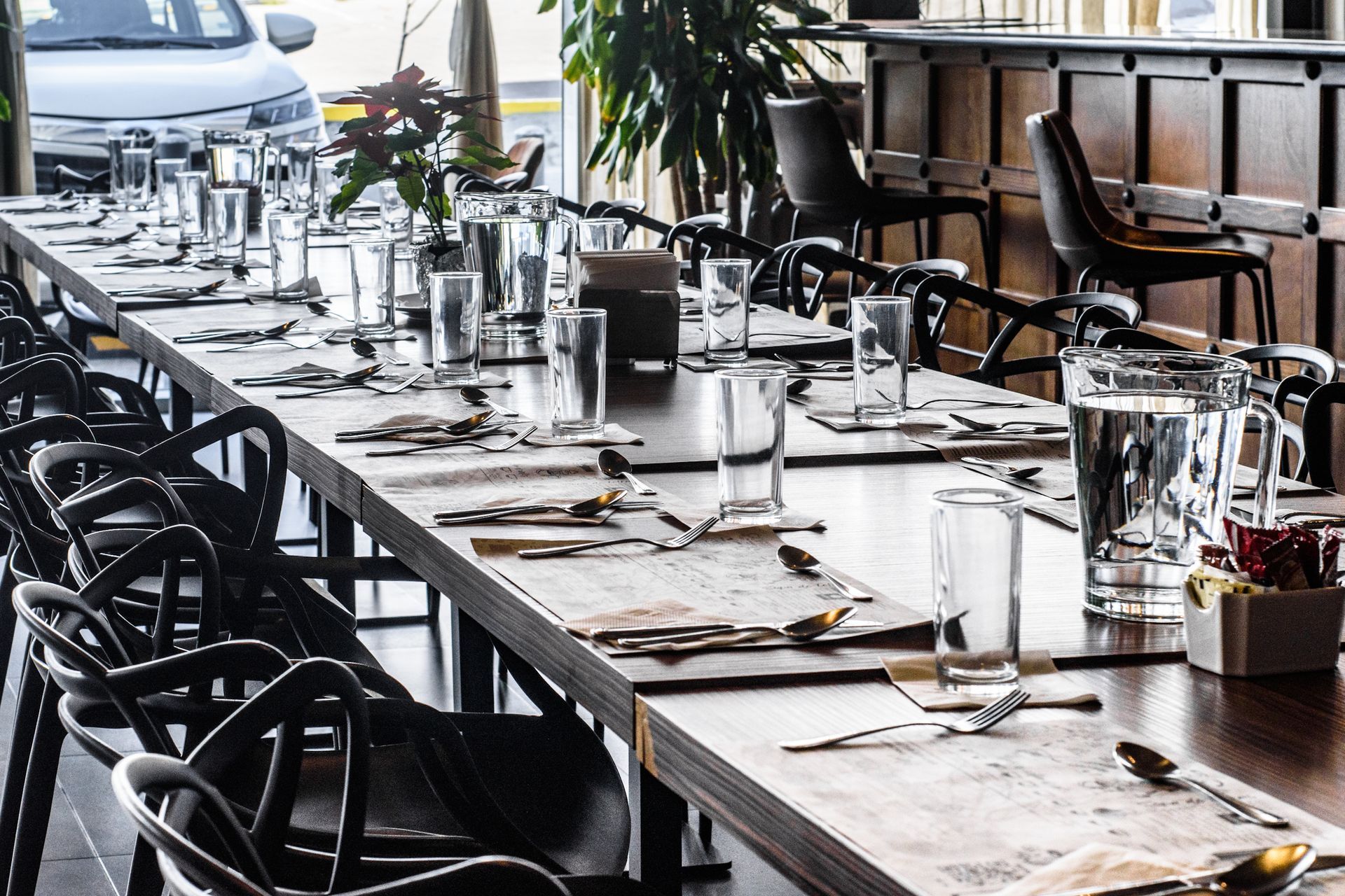 Mesa de comedor larga puesta para invitados en un restaurante con vasos de agua y cubiertos.