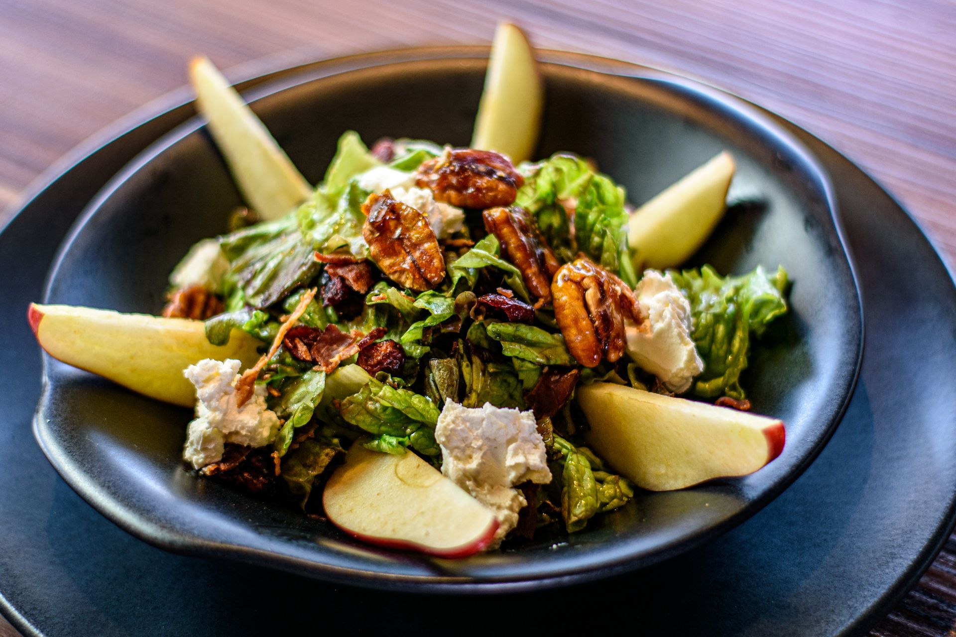 Ensalada con manzanas, nueces, lechuga y queso de cabra en un recipiente negro.