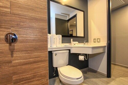 Baño con azulejos imitación madera, inodoro, lavabo, espejo y espacio accesible para el lavabo. Mando de ducha visible.