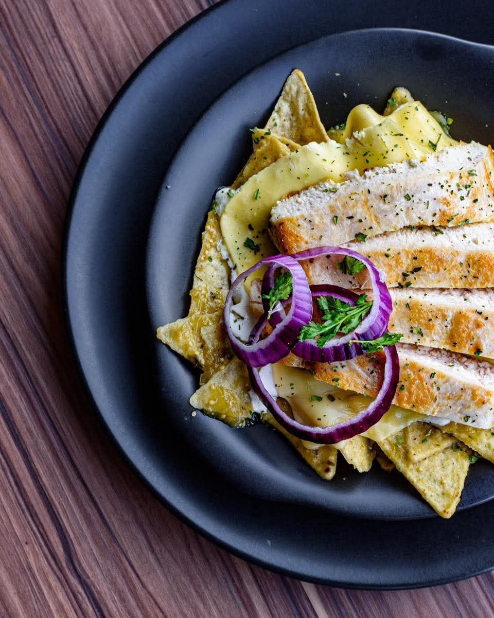 Pollo y nachos en platos negros, cubiertos con cebolla roja y hierbas, sobre una superficie de madera.