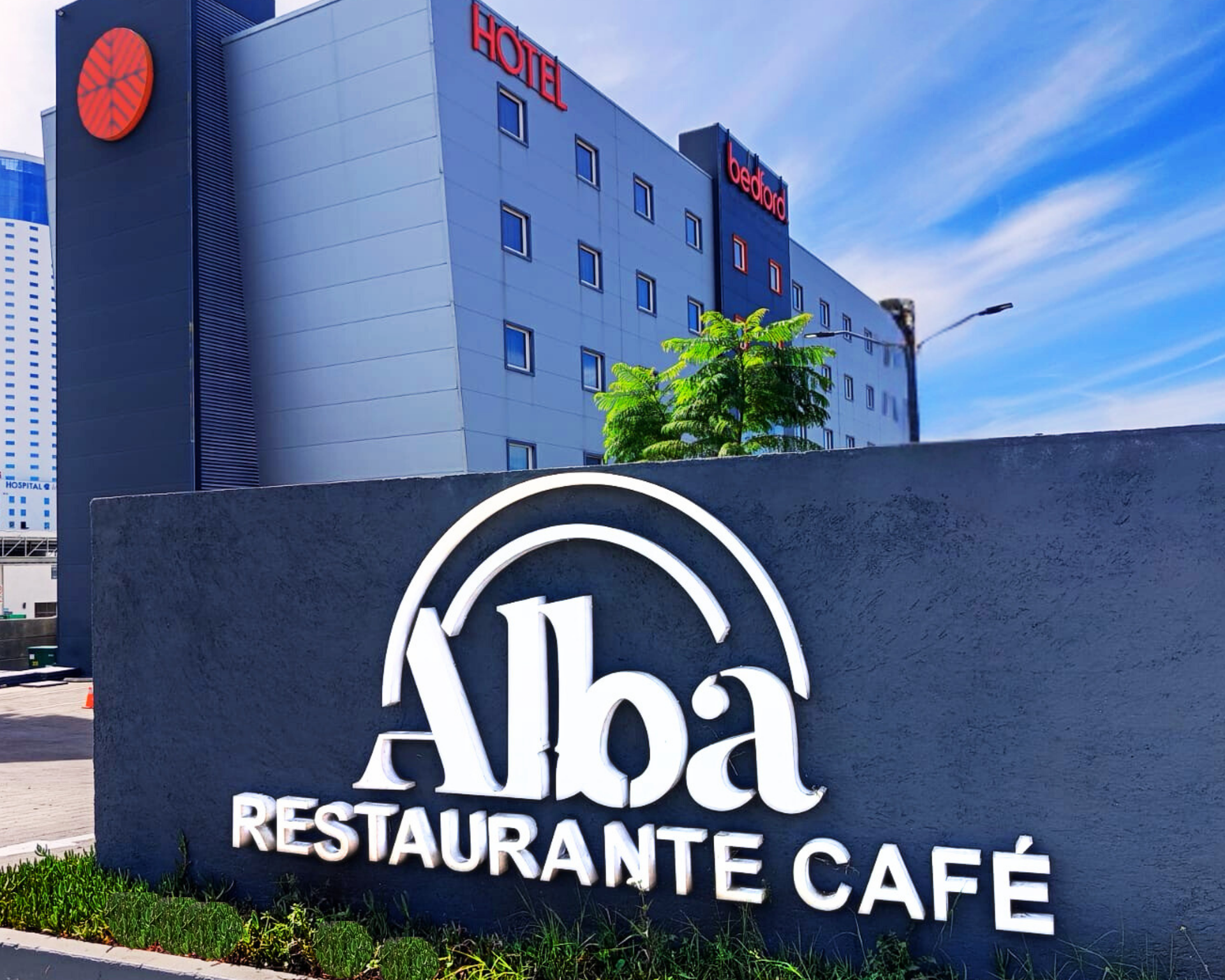 Letrero de Alba Restaurante Café frente a un moderno edificio de hotel bajo un cielo azul.