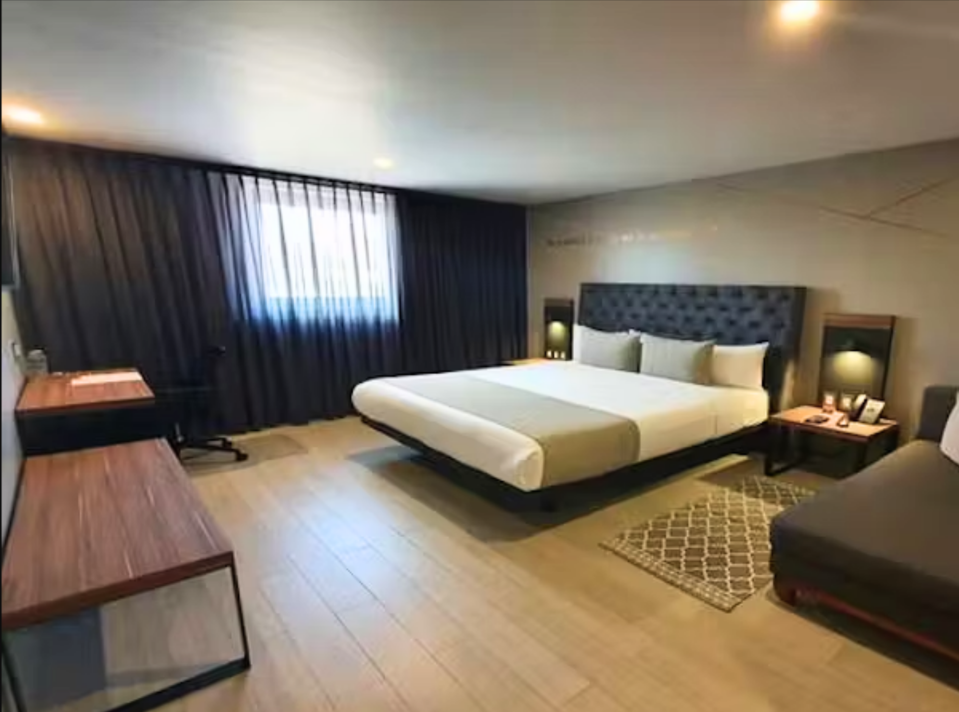 Habitación de hotel con cama King, escritorio, sofá, suelo de madera y cortinas oscuras.