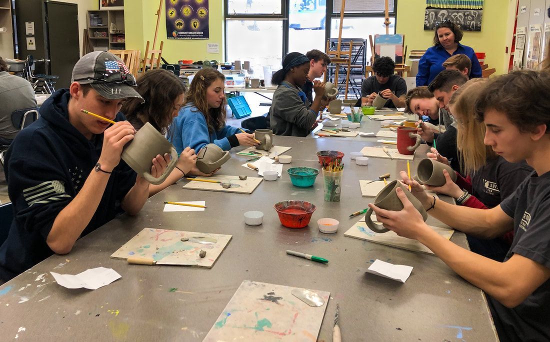 a group of people are sitting around a table making pottery .