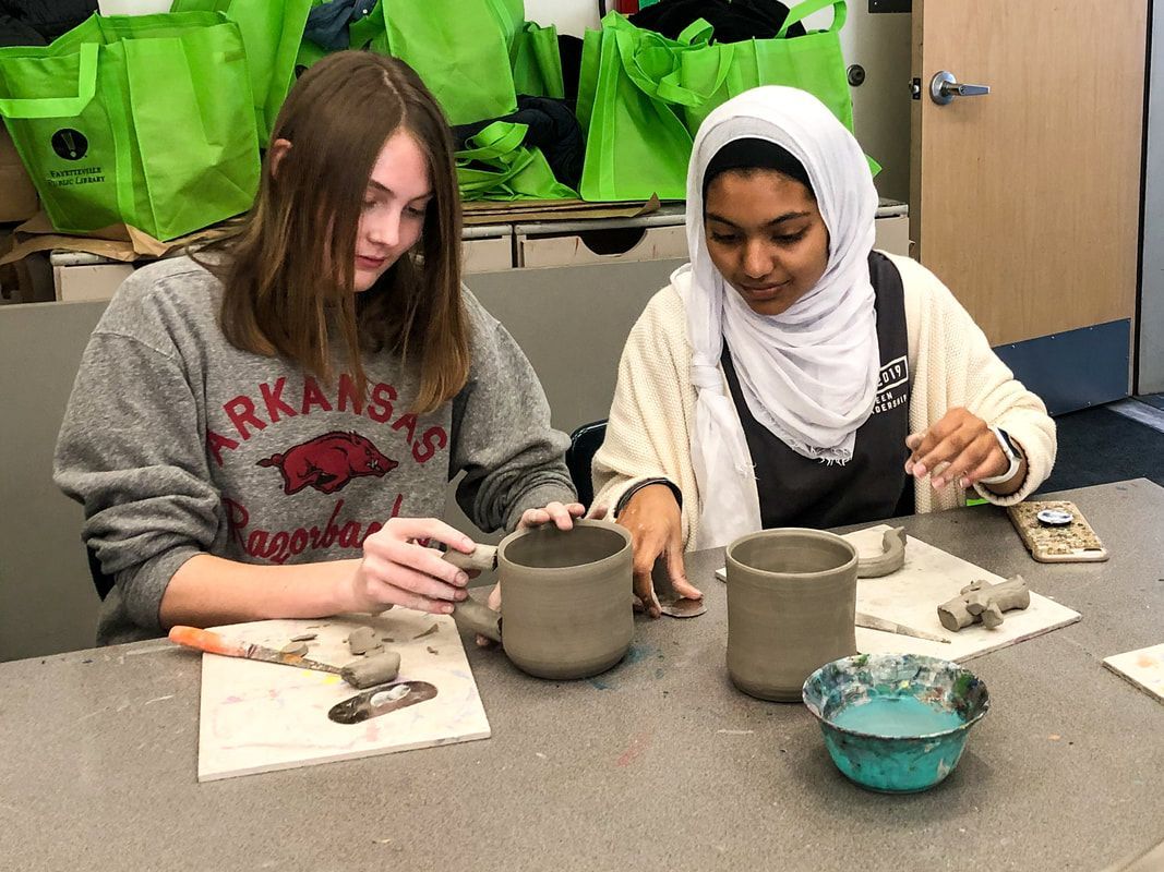 two girls are sitting at a table making clay pots .