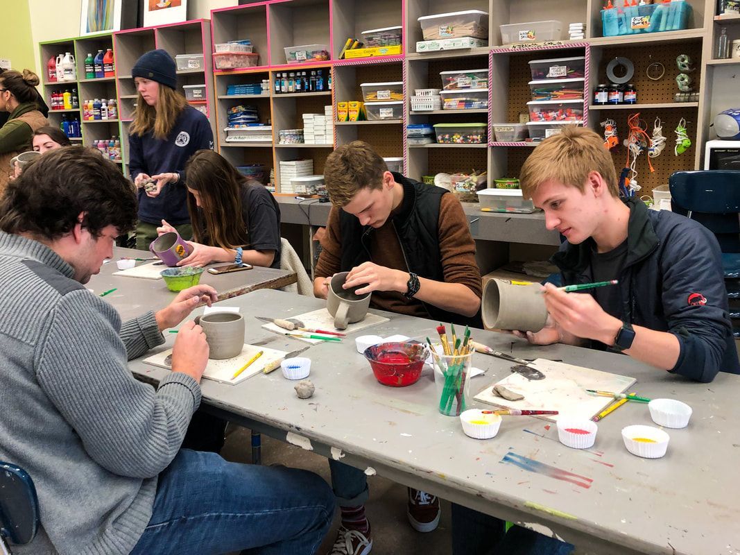 a group of young people are sitting at a table making pottery .