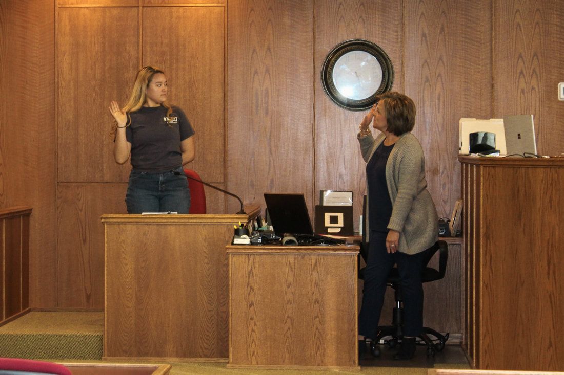 two women are standing in front of a clock in a courtroom .