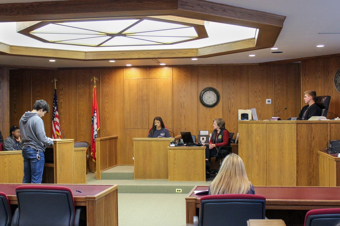 a man is standing in front of a judge in a courtroom .