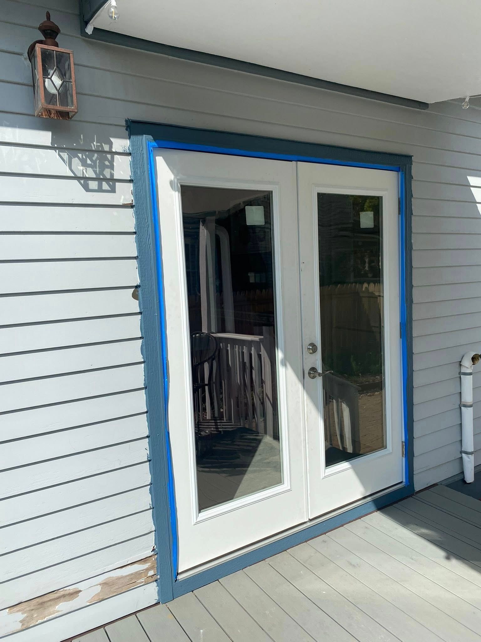 Exterior French doors, painted white, with blue painter's tape; on a gray-sided building with a porch.