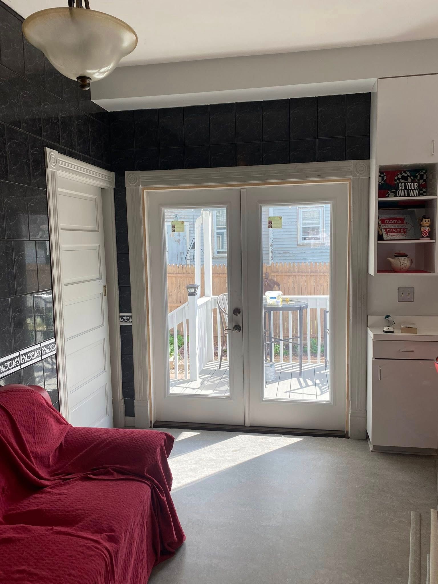 Red sofa in a kitchen with French doors to a wooden deck. Black backsplash.