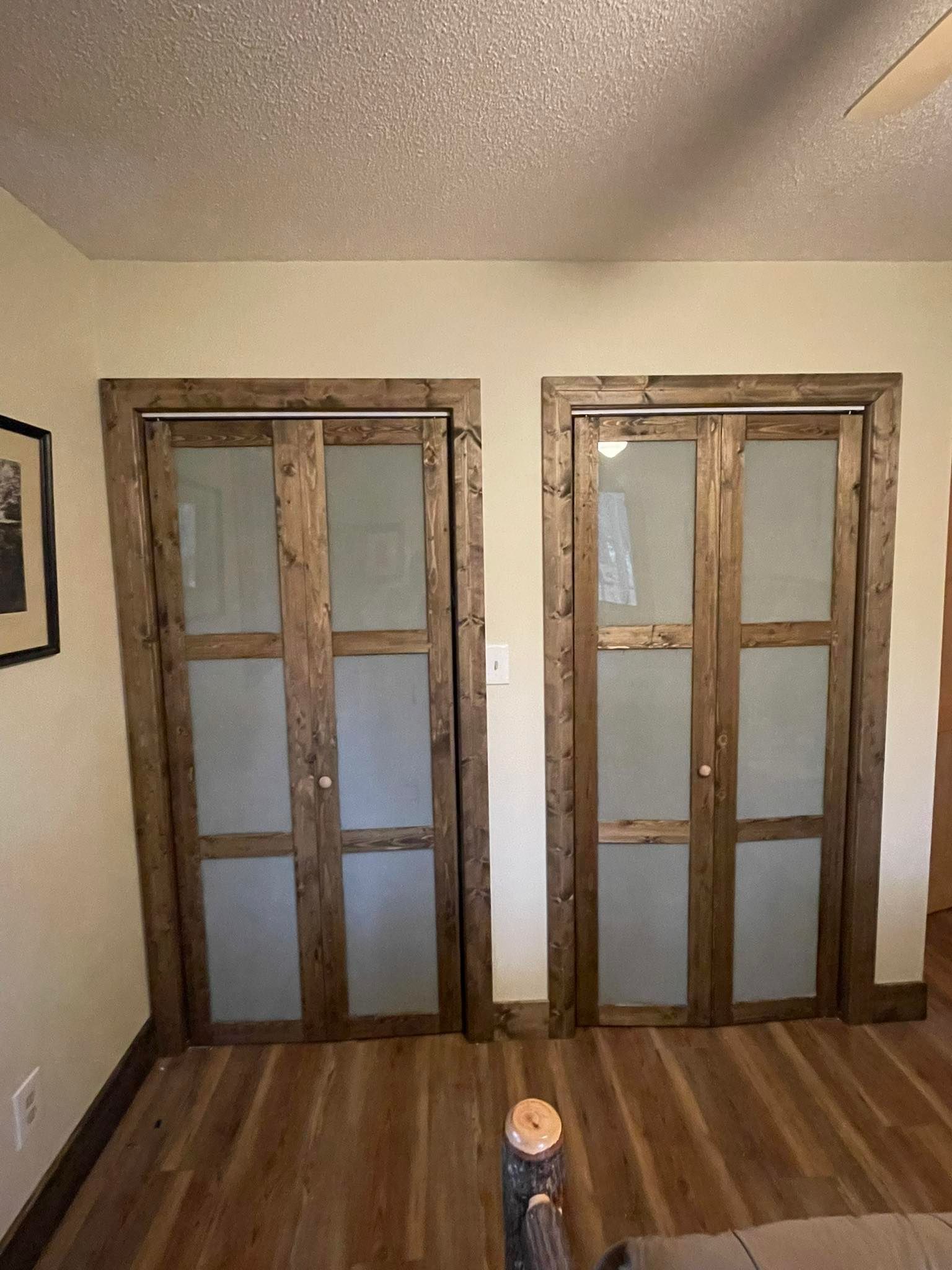Two rustic wooden closet doors with frosted glass panels, set in a light-colored room.
