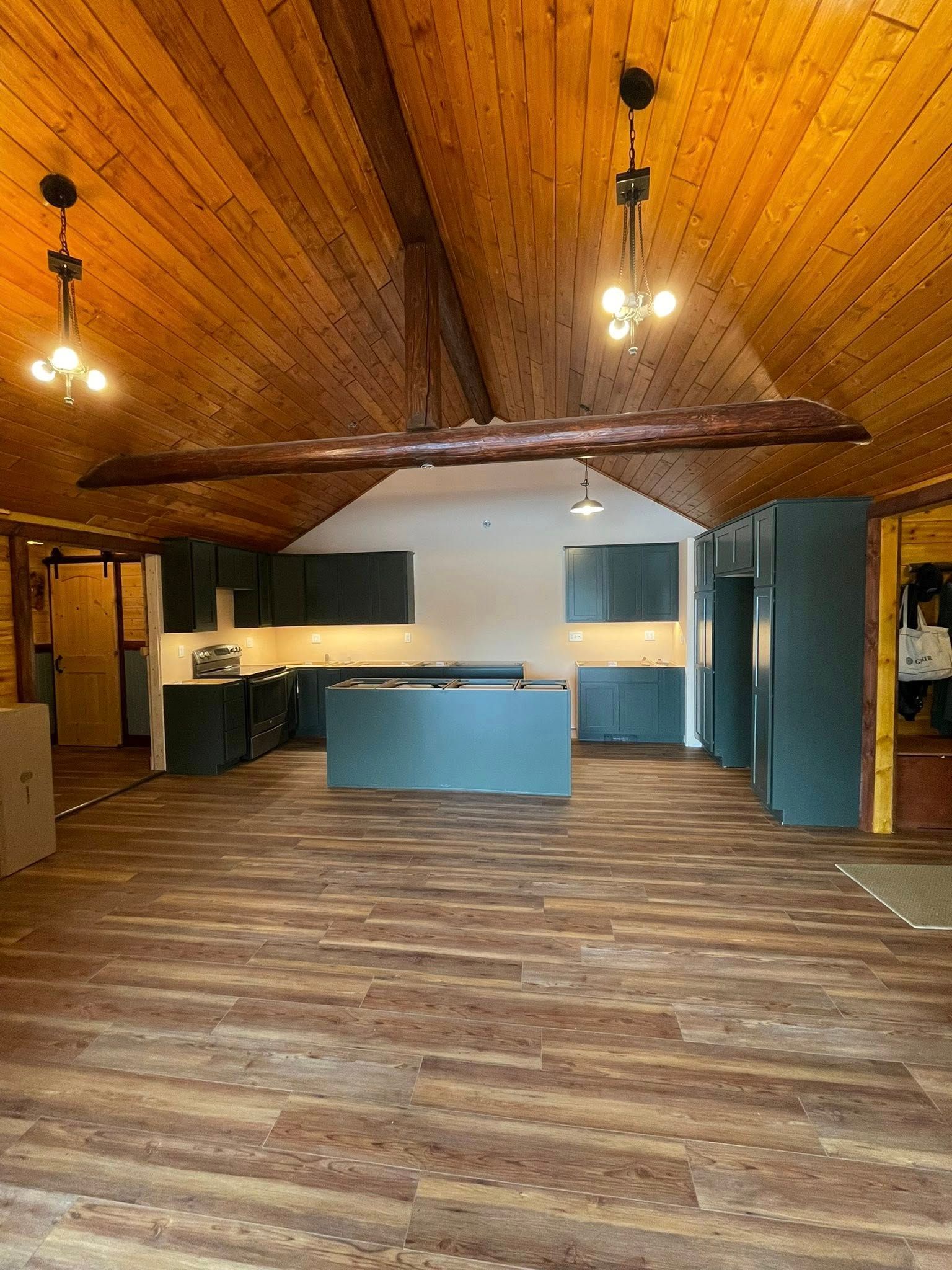 Wooden-floored kitchen with dark cabinets. Light fixtures hang from a sloped wooden ceiling.