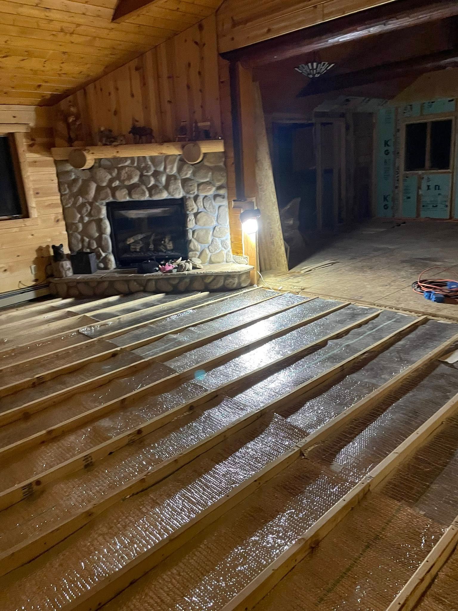 Wooden floorboards laid out in a room, with a stone fireplace in the background. Construction in progress.