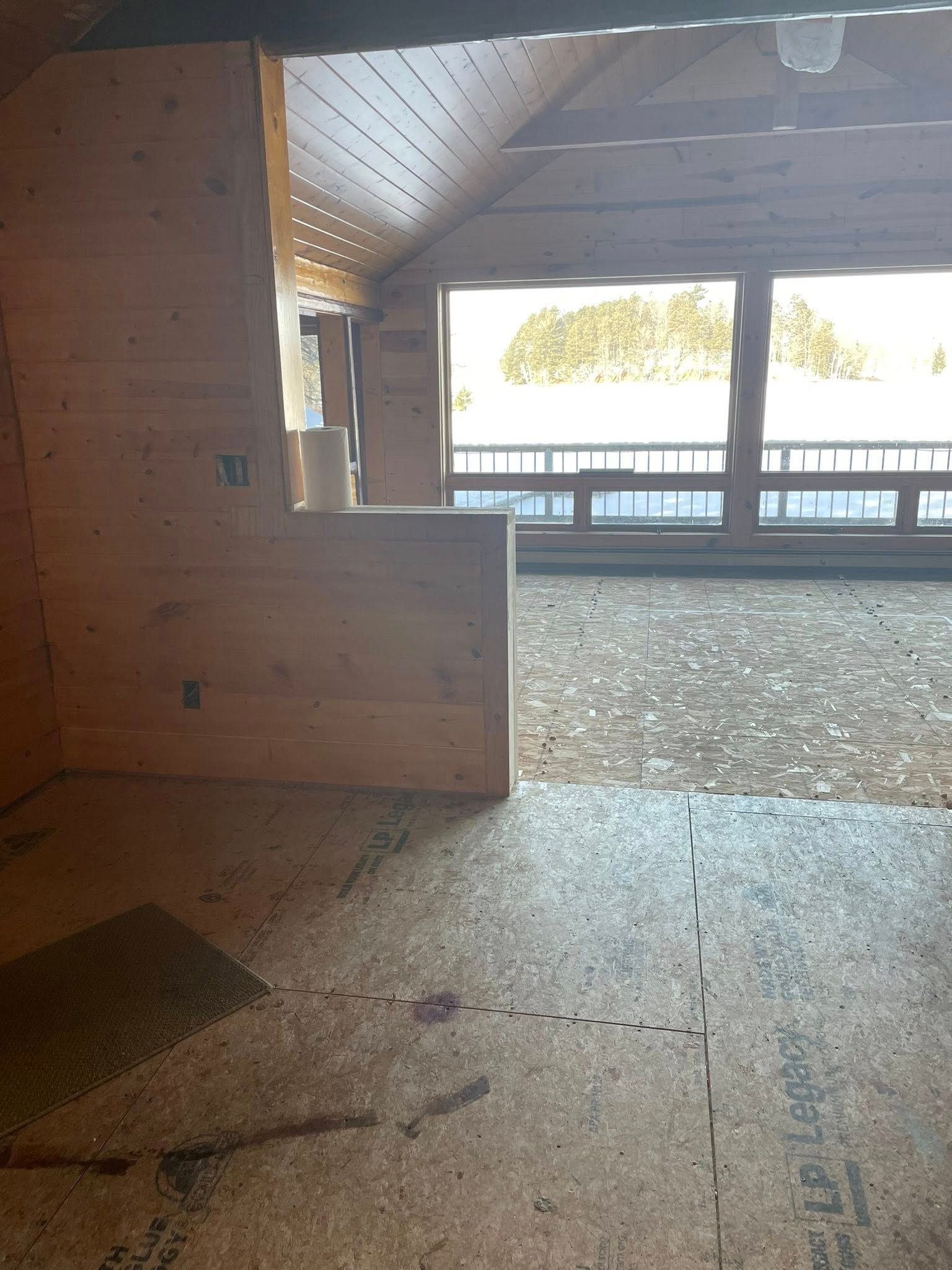 Interior of a room under construction with wood paneling and a large window looking out onto a snow-covered landscape.