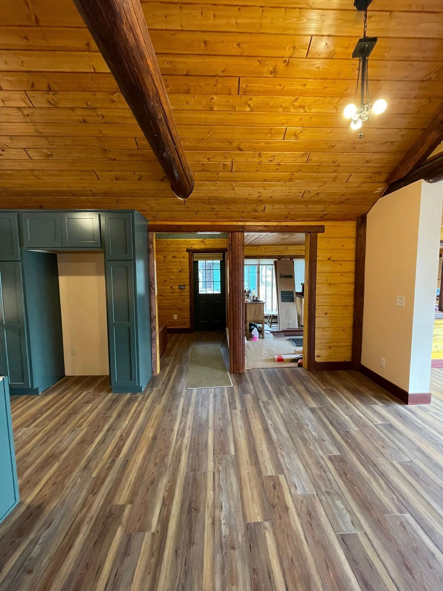 Interior view: wooden ceiling, wood floor, green cabinets, and doorway leading to another room.