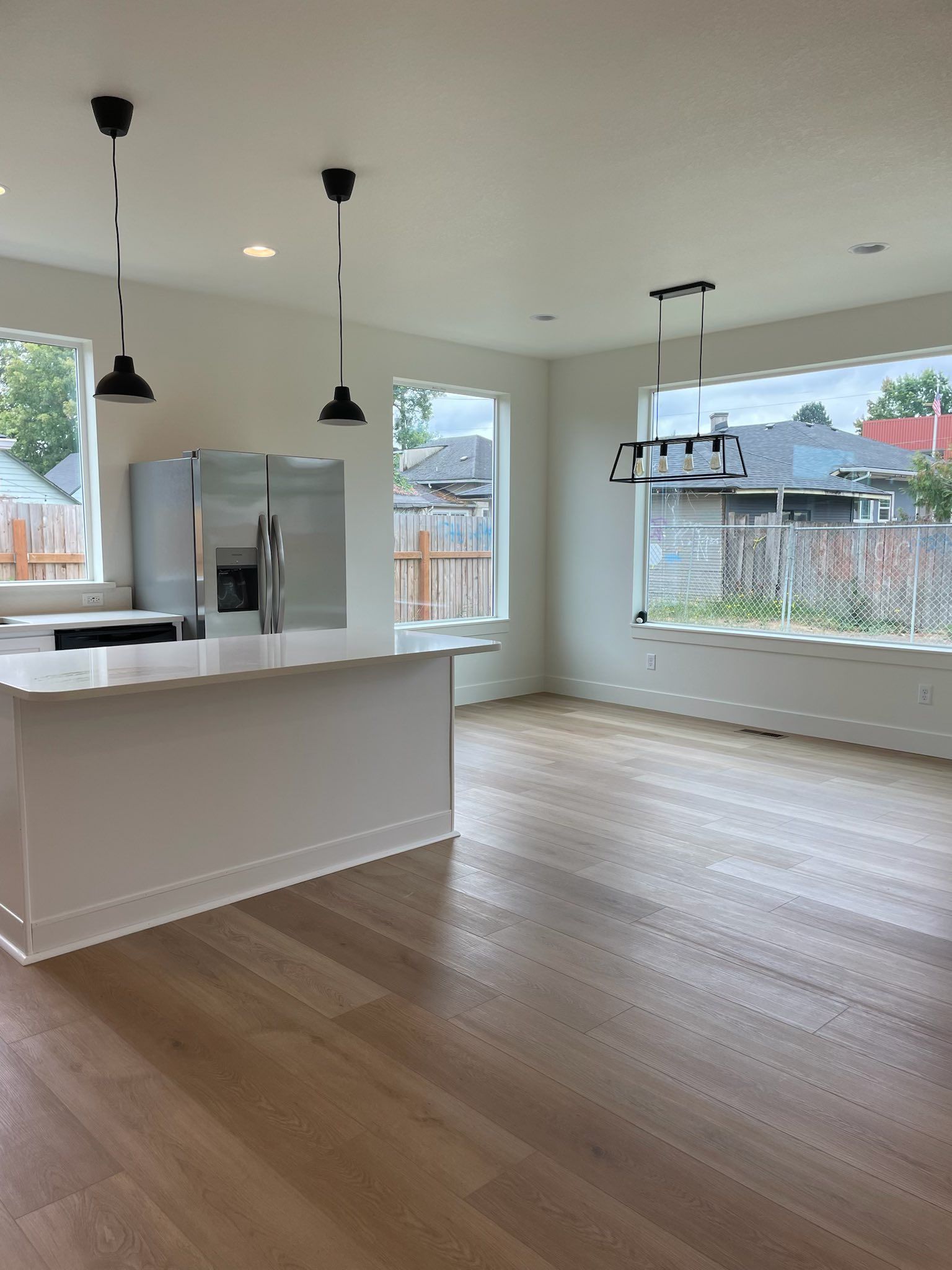 Bright kitchen with white island, stainless steel fridge, wood floors, and black pendant lights.