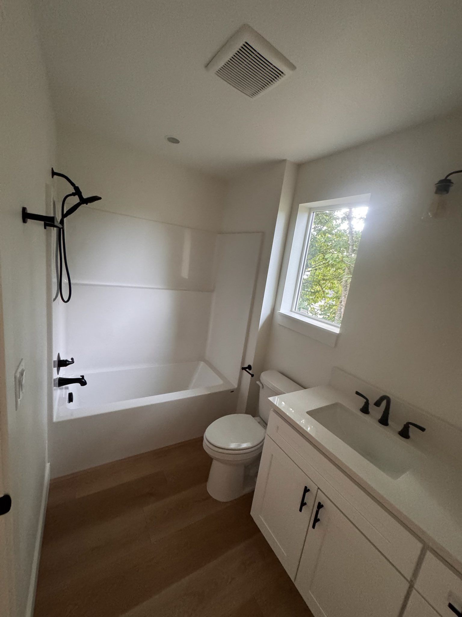 Bathroom with white walls, black fixtures, and wood-look flooring. Includes tub/shower combo, vanity, and toilet.