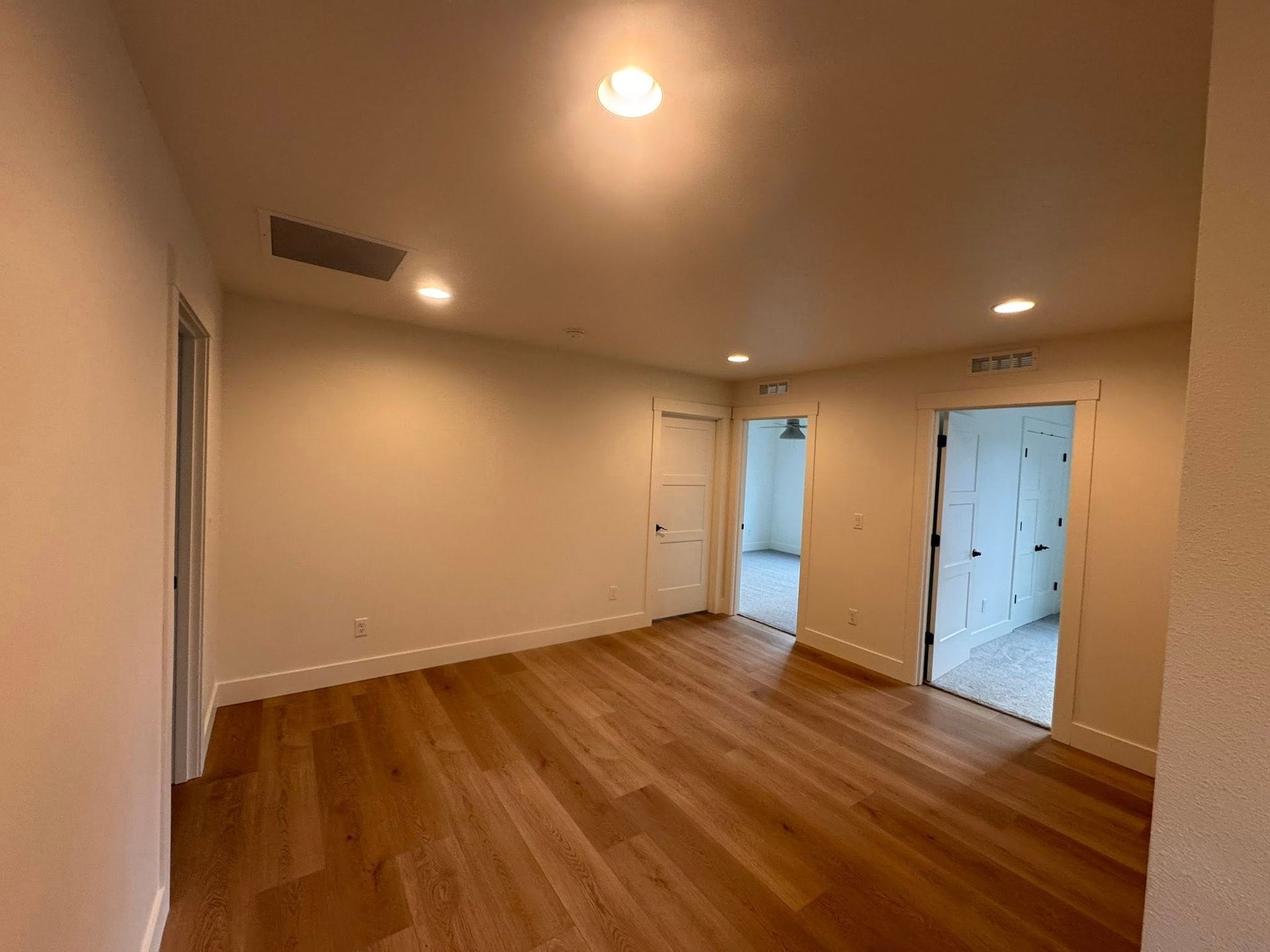 Empty room with hardwood floors, three doors, and recessed ceiling lights.