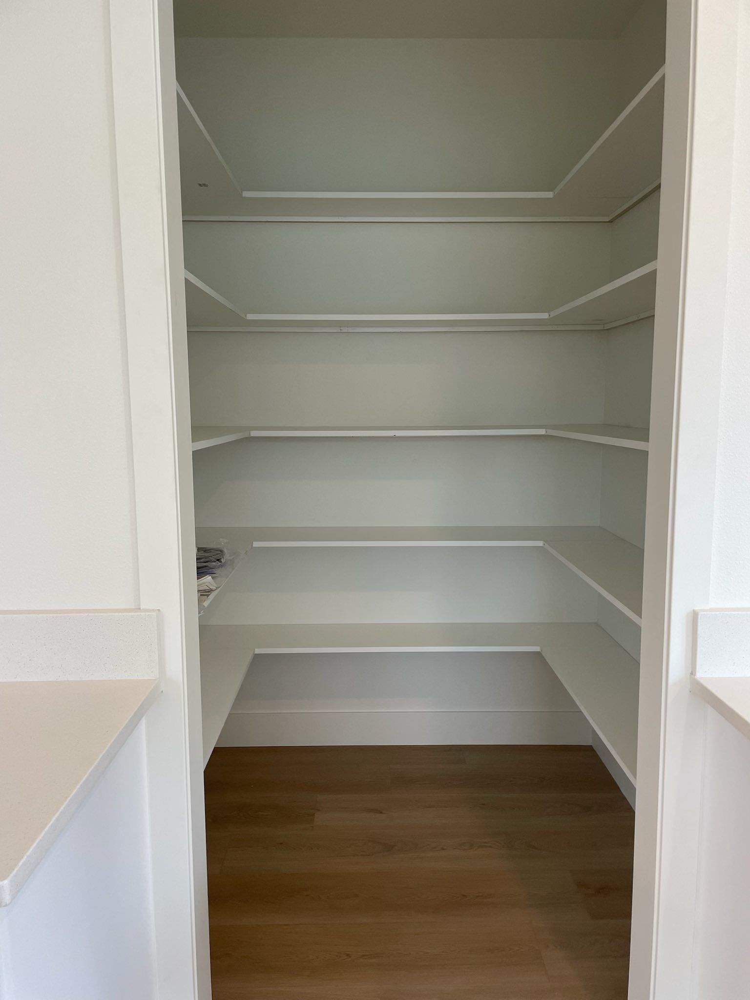 Empty white pantry with multiple shelves; wood floor.