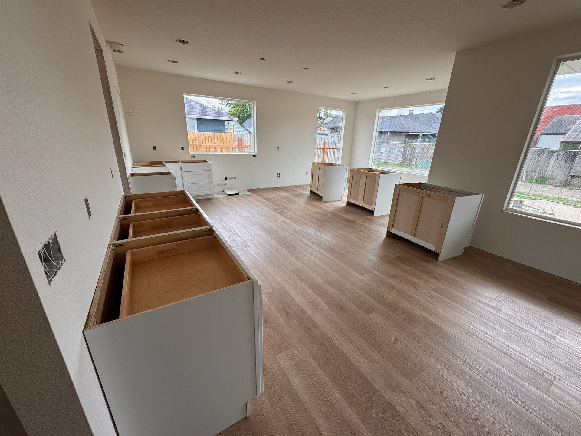 Kitchen under construction with unfinished cabinets and wood-look flooring.