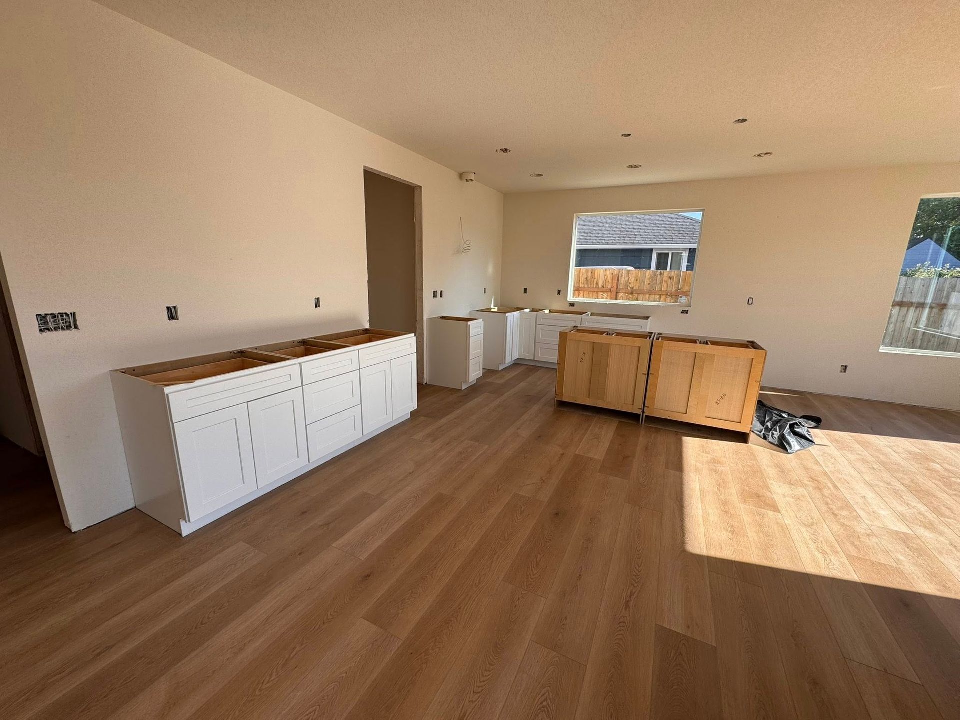 Kitchen under construction with white cabinets, wood floor, and windows.
