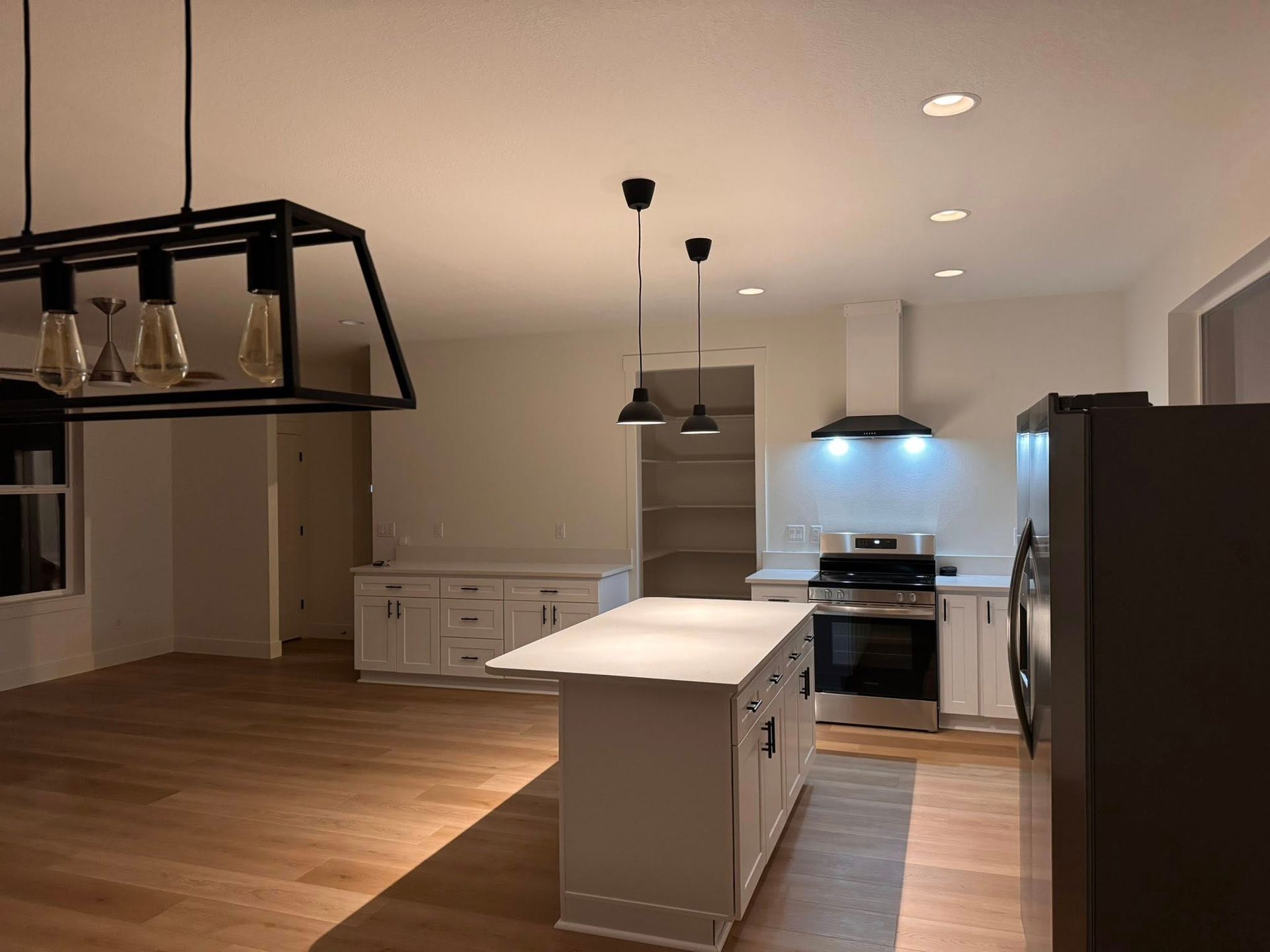 Modern kitchen with white cabinets, island, and stainless steel appliances. Hardwood floors and pendant lights.